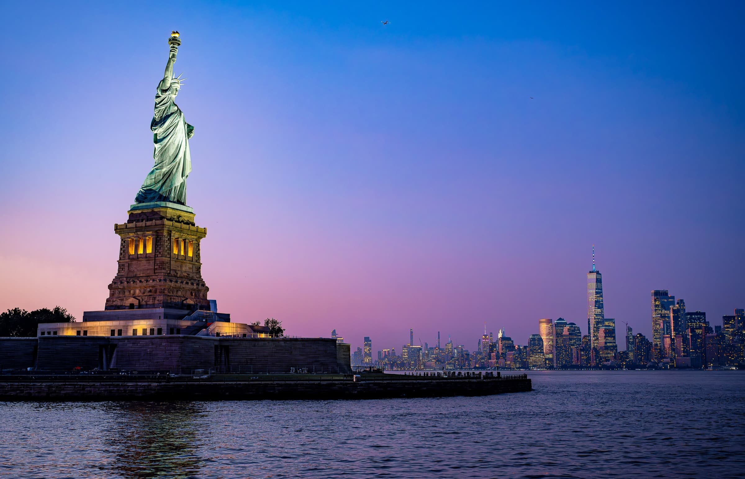 The Statue of Liberty lit at dusk, seen from a cruise in New York Harbor